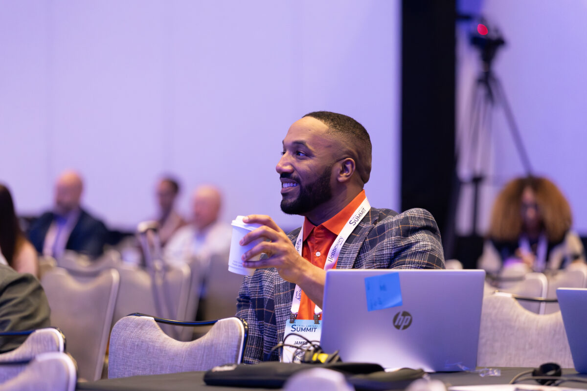 Conference attendee smiling while holding a coffee cup and seated with a laptop during the Trial Lawyers Summit.